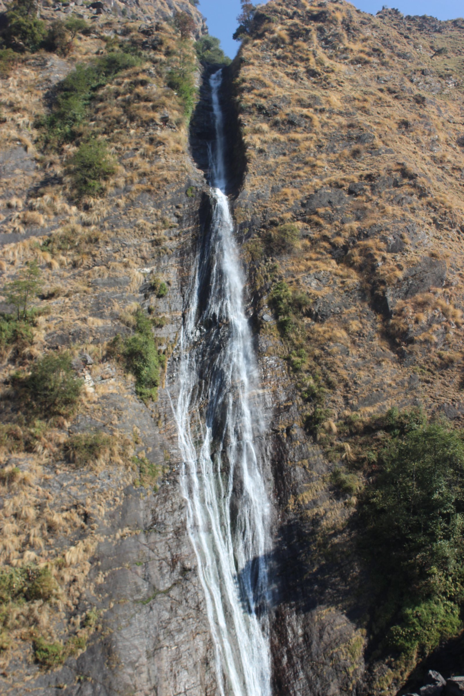 Birthi Falls dropping in a narrow white ribbon down a steep, grassy Himalayan cliff face