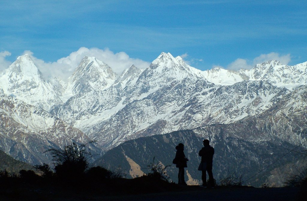 Two visitors silhouetted against the snow-capped Panchachuli range from a viewpoint near Munsiyari