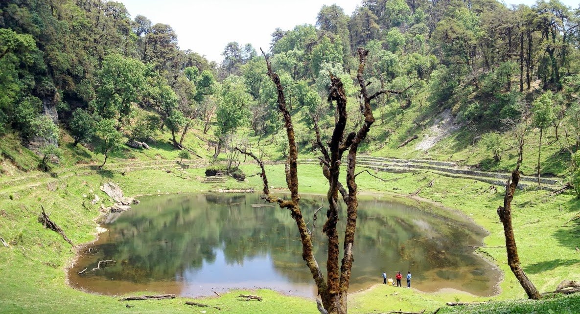 Visitors standing at the edge of Thamri Kund lake, surrounded by green forest and meadow